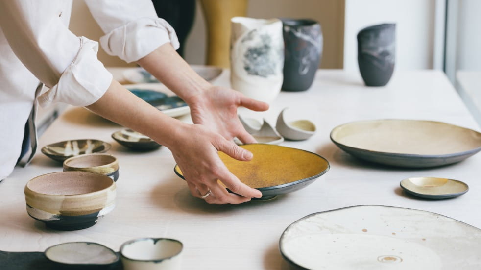 woman placing plate on table of ceramics